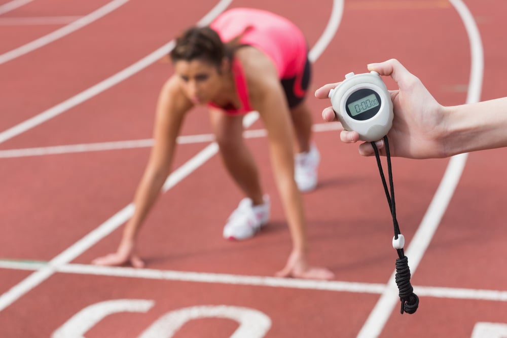 Close-up of a hand timing a blurred young womans run on the running track